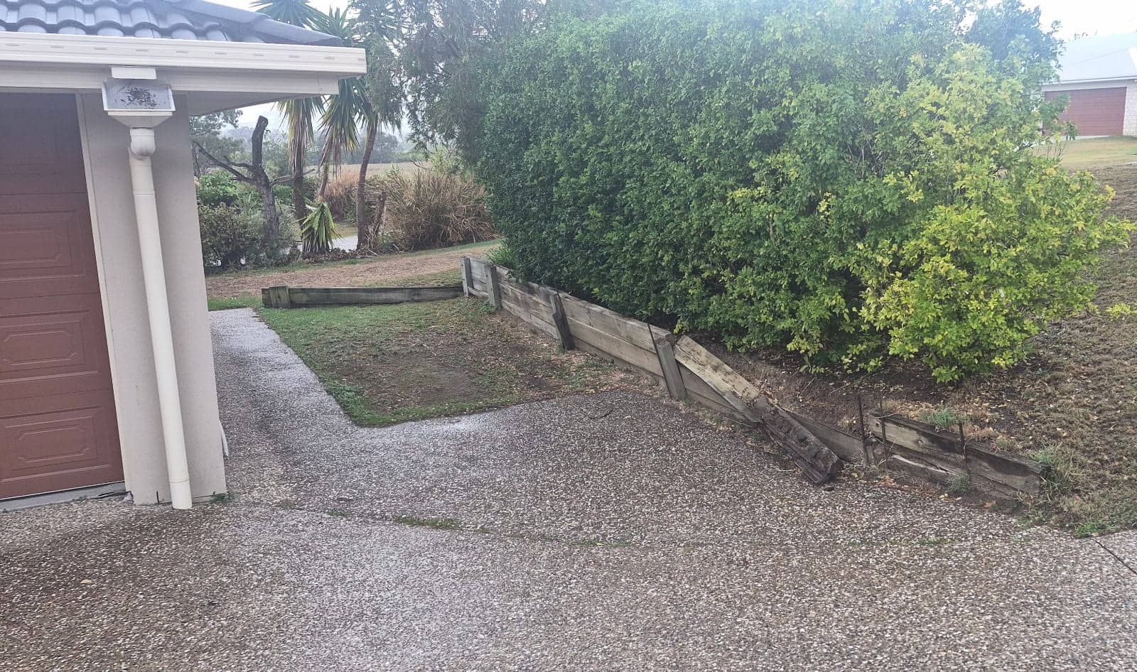 The old timber wall beside the garage, broken and sagging onto the driveway
