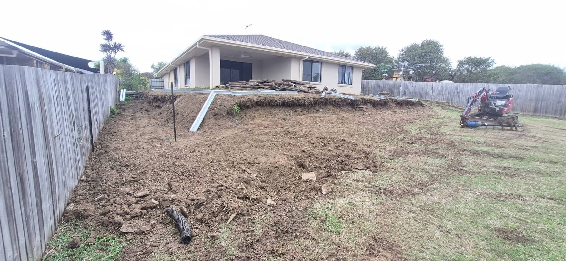 The back yard with the old wall gone and the ground dug out, a small excavator on the lawn