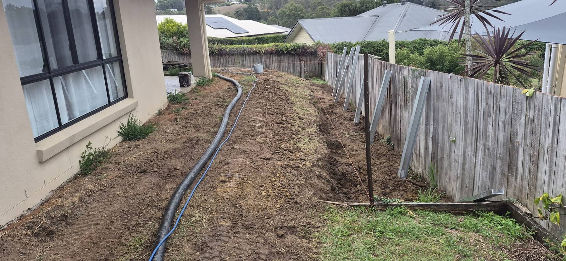 The side of the house with the line dug out along the fence and new steel posts leaning on it