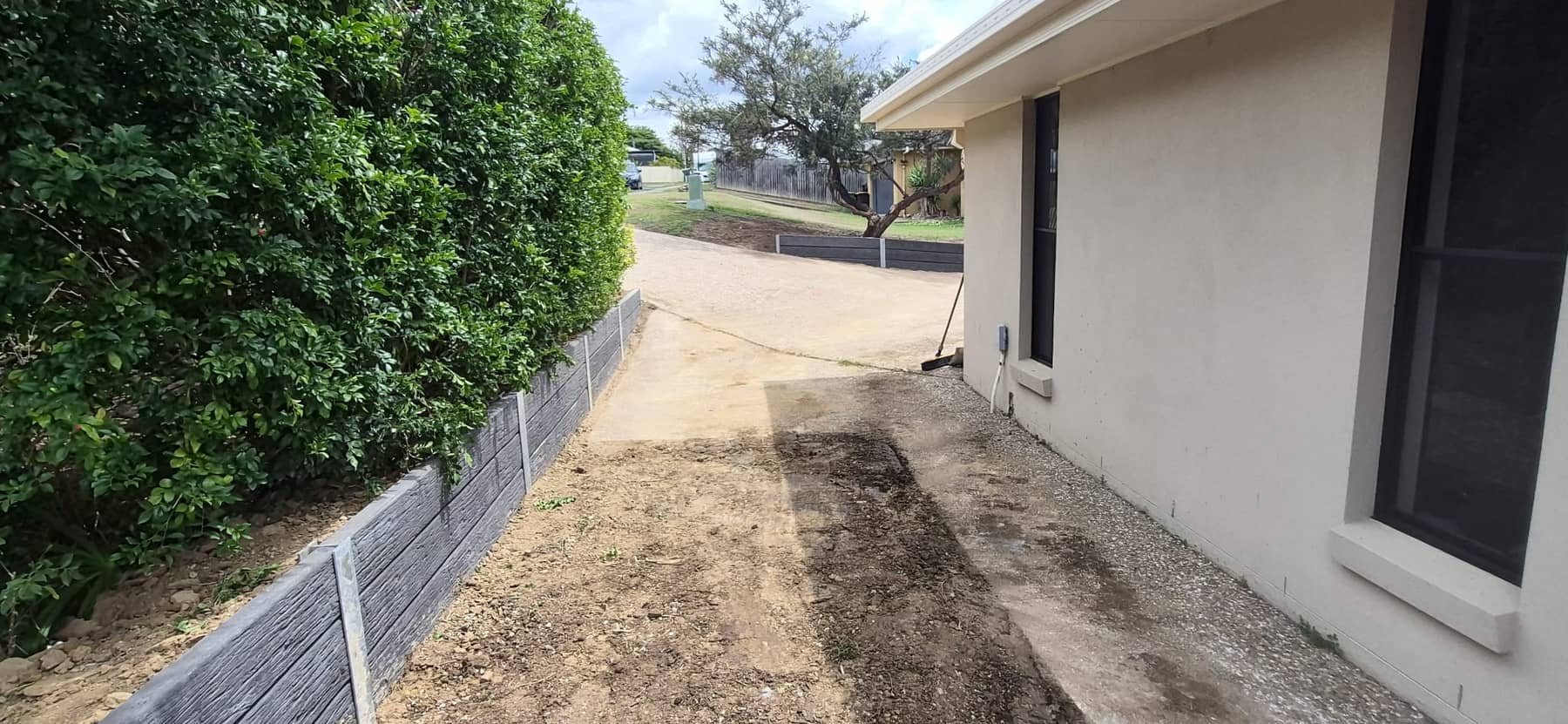 The finished concrete sleeper wall beside the garage, along the hedge