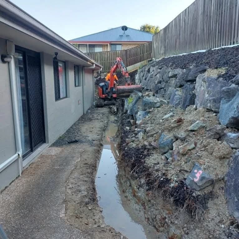 An excavator digging along the side access beside the house